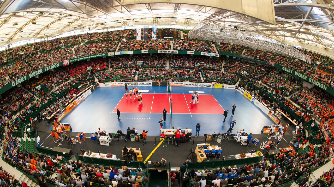 Volleyballspiel in einer vollen Halle, zwei Teams stehen auf dem Spielfeld.