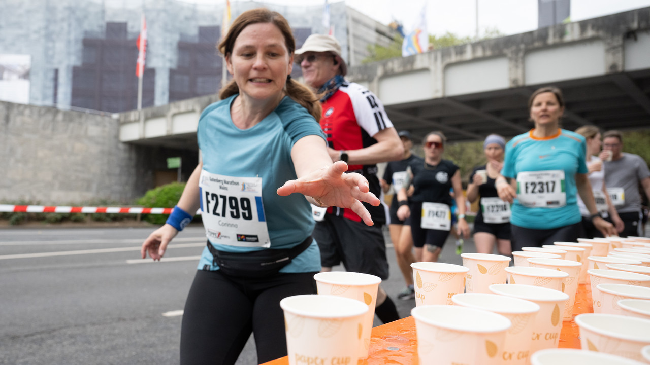 Läuferin greift während eines Marathons nach einem Pappbecher mit Wasser an einer Versorgungsstation.