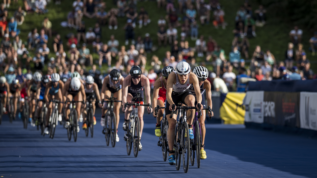 Gruppe von Triathletinnen fährt konzentriert nebeneinander mit Fahrrädern auf blauer Strecke.
