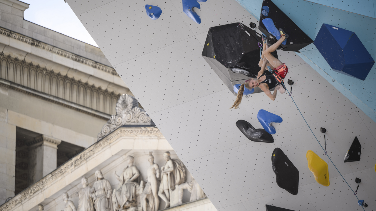 Kletterin hängt kopfüber an bunten Griffen einer überhängenden Kletterwand.