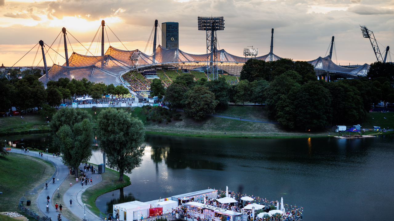 Abendliche Aufnahme des Olympiastadions mit Zuschauern und Festival am Seeufer.