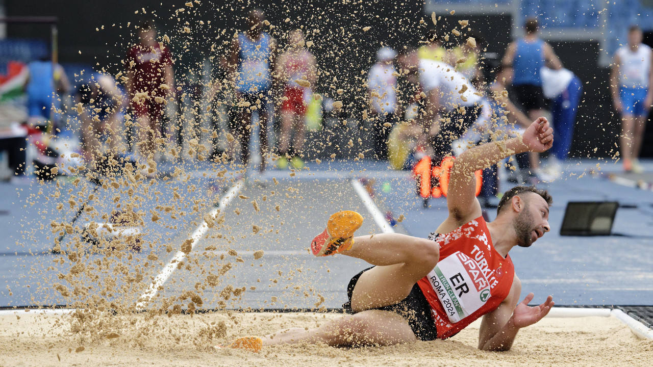 Leichtathlet landet beim Weitsprung im Sand, während Sandkörner in die Luft spritzen.