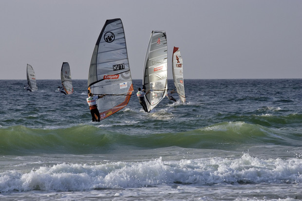 Mehrere Windsurfer mit Segeln fahren auf dem Meer bei leichten Wellen.