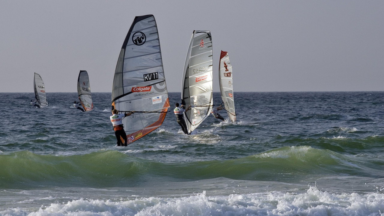 Mehrere Windsurfer mit Segeln fahren auf dem Meer bei leichten Wellen.