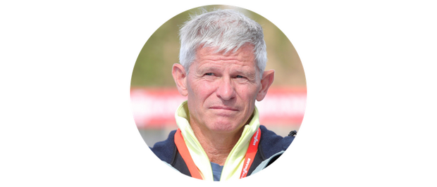 Porträt von Hubert Schwarz, der in die Ferne schaut. Er hat graue Haare und trägt eine dunkelblaue Jacke mit einem orangefarbenen Band um den Hals.