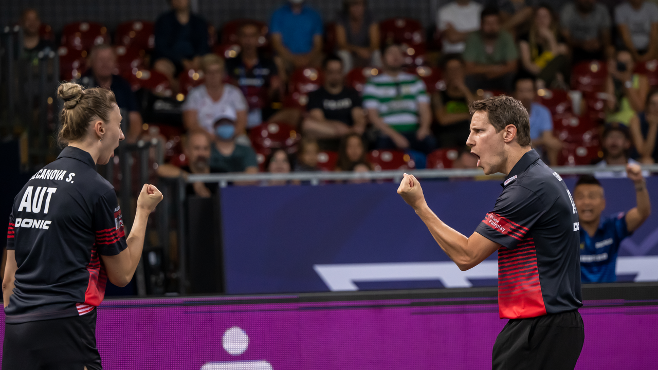 Zwei österreichische Tischtennisspieler jubeln während eines Mixed-Doppel-Matches bei den European Championships 2022 in München. Beide zeigen kämpferische Gesten nach einem Punktgewinn.