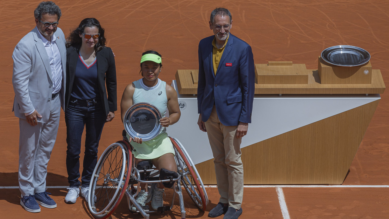 Rollstuhl-Tennisspielerin hält einen Siegerpokal auf dem Sandplatz, neben ihr stehen drei Offizielle.