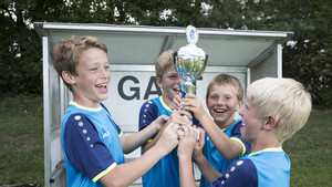 Vier Kinder im blauen Trikot jubeln und halten gemeinsam einen Pokal hoch.