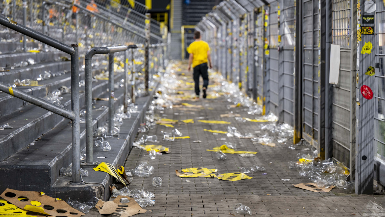Leere Tribüne im Stadion mit Müll und Bechern auf dem Boden, eine Person in Gelb läuft davon.
