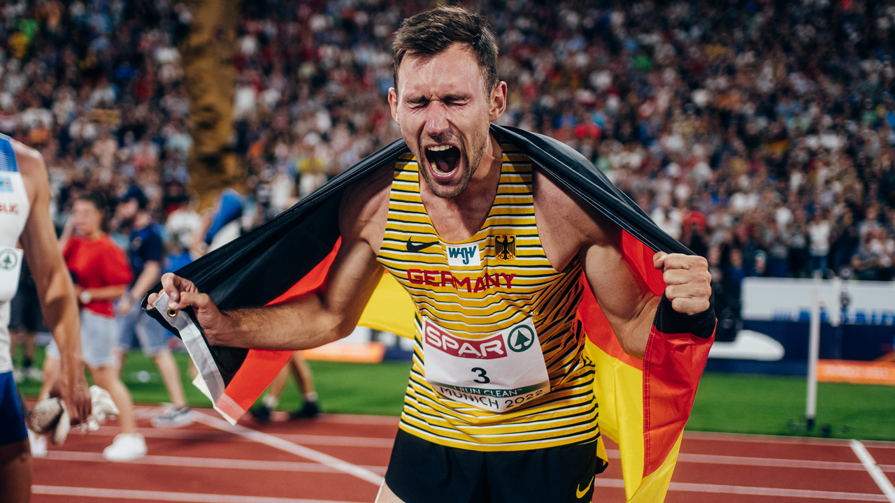 Leichtathlet jubelt mit deutscher Flagge lautstark im Stadion nach dem Wettkampf.