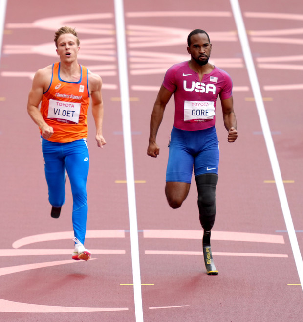 Drei Para-Leichtathleten mit Prothesen sprinten auf der Laufbahn bei einem Wettkampf.