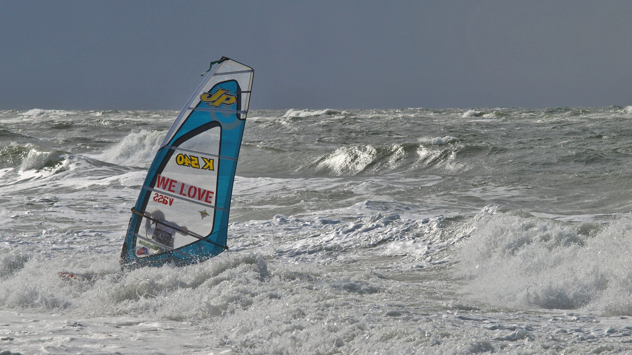 Windsurfer kämpft sich bei starkem Wellengang durch die raue See.