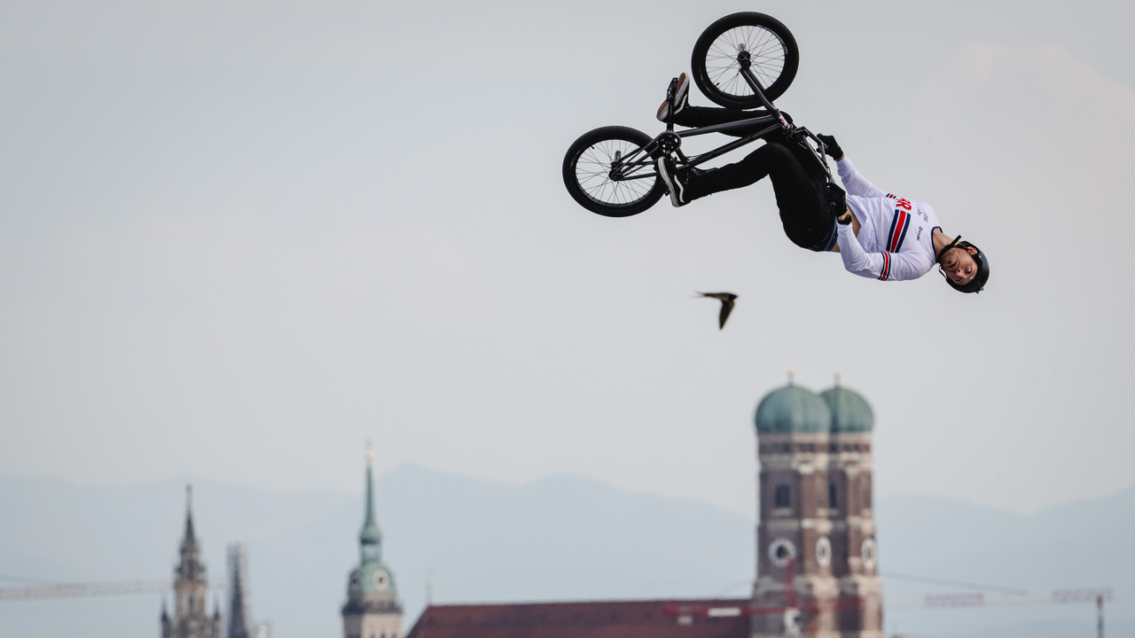 BMX-Fahrer macht einen Rückwärtssalto hoch über der Stadt mit Kirchtürmen.